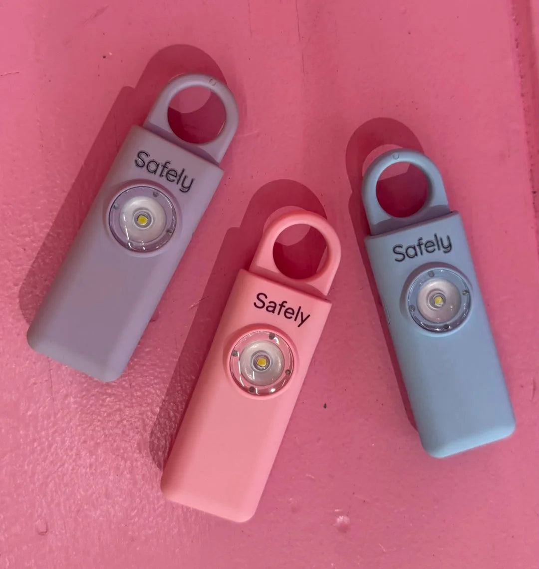שלושה מכשירי Safely בצבעים ורוד, תכלת ואפור־לילך על משטח ורוד